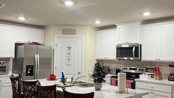 A modern kitchen with white cabinets, stainless steel appliances, a marble countertop, and a central island with bar stools.