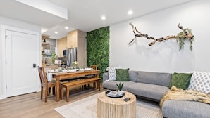 Un salon moderne comprenant un coin repas, un canapé gris, une table basse en bois et un mur décoratif vert.