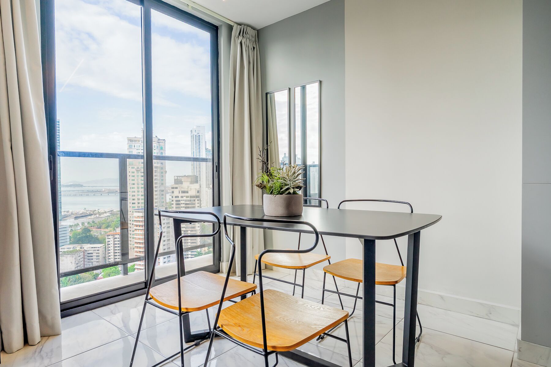 Una habitación moderna con un ventanal grande, una mesa con sillas y una planta en maceta.