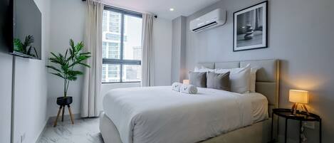 A modern hotel room with a large bed, a potted plant, a flat-screen TV, and a city view.
