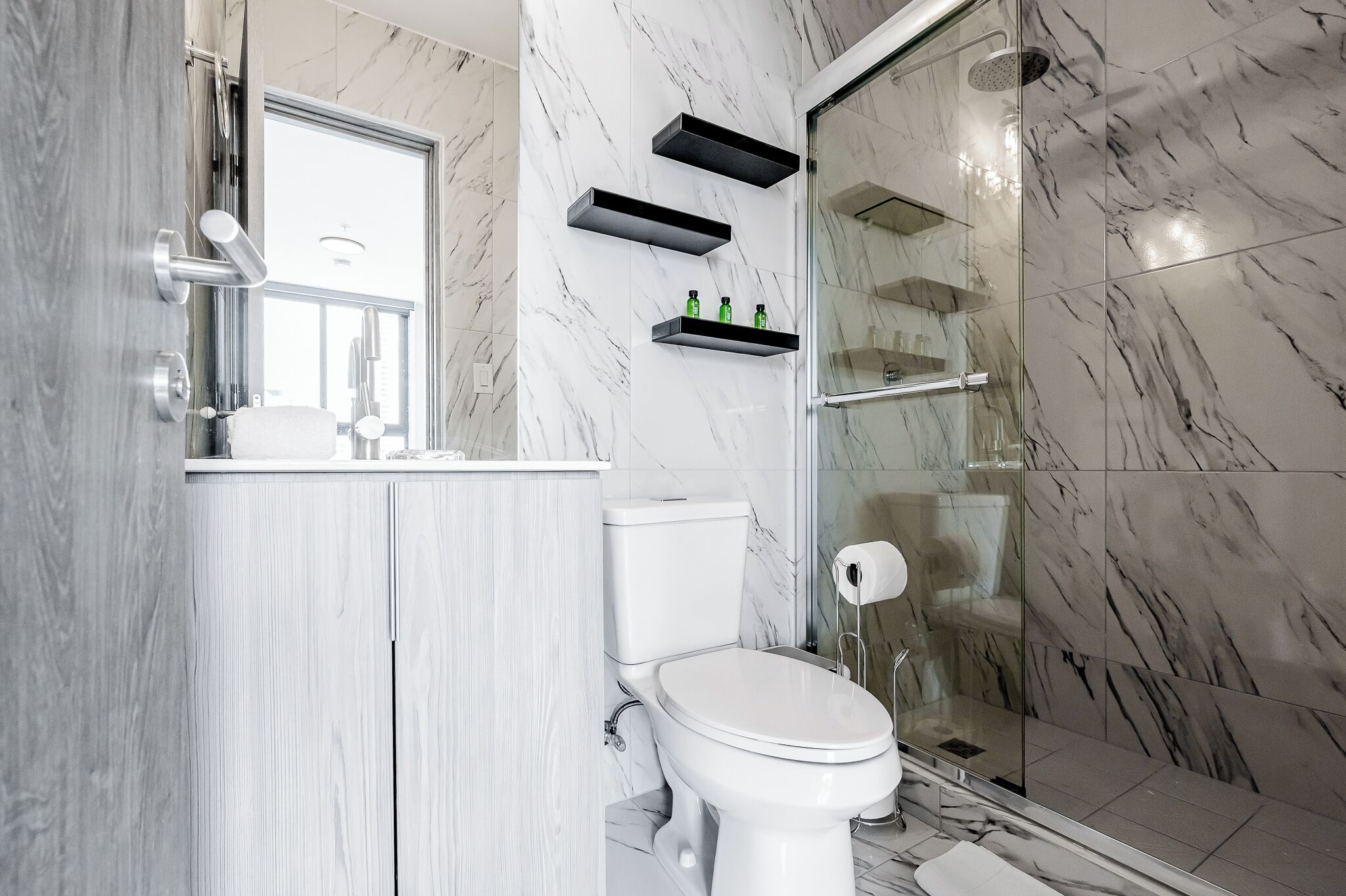 Ein modernes Badezimmer mit Toilette, Marmorwänden, einer Duschkabine aus Glas und Einbauregalen.