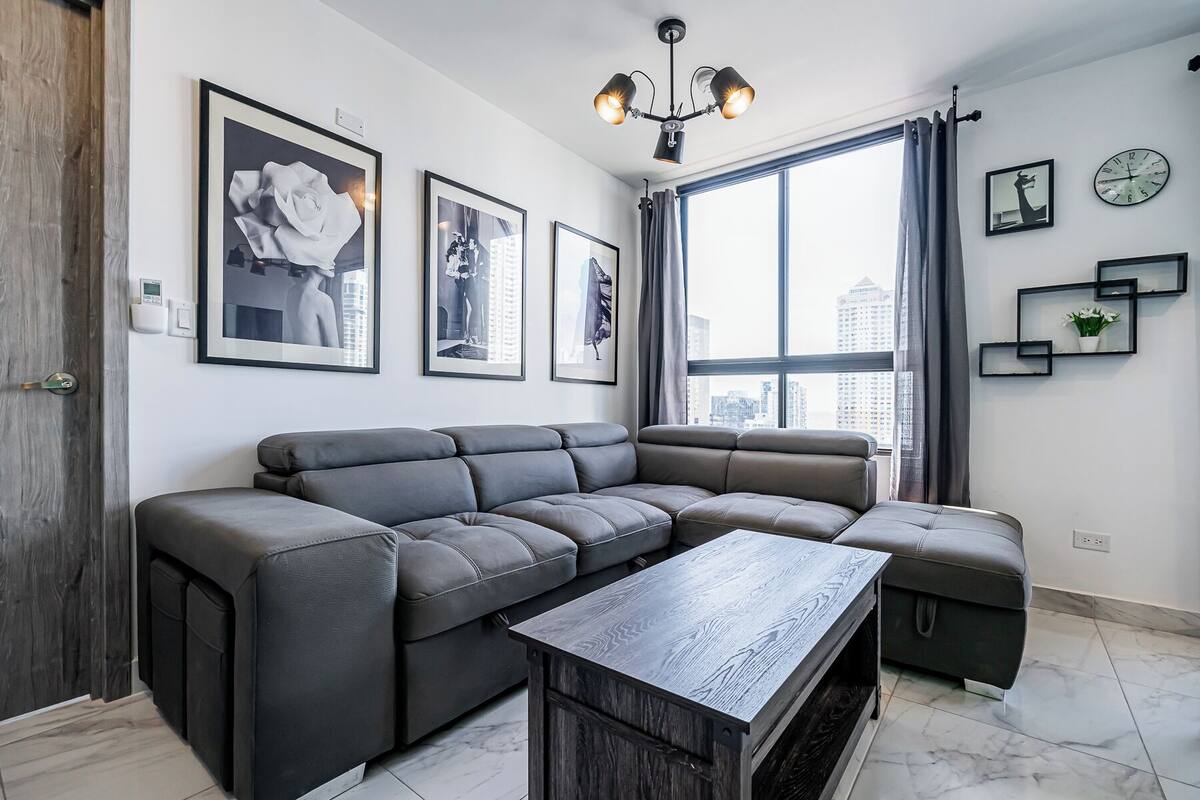 Ein modernes Wohnzimmer mit einer Eckcouch, einem Holztisch und Blick auf die Stadt durch große Fenster.