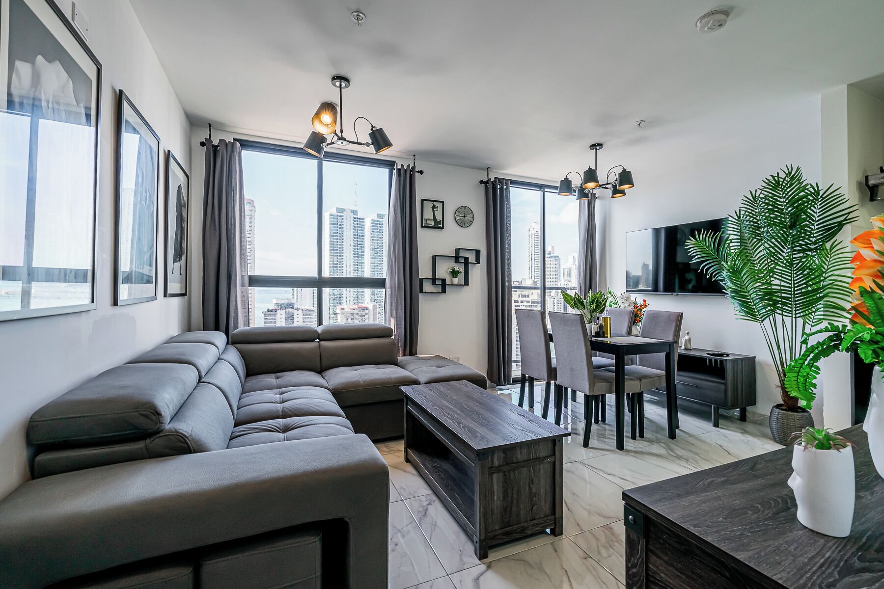 Una sala moderna con un sofá seccional, una mesa de comedor con sillas, una mesa de centro y un televisor montado en la pared.
