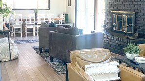 A spacious living room with a high ceiling, a fireplace, and a dining area with white furniture.