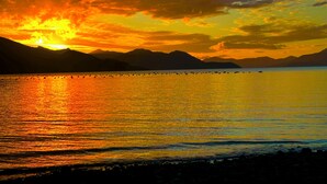 A sunset over a calm lake with mountains in the background. - Remote Pelorus Sound Kiwi Bach on the Beach with Great Views (Totaranui)