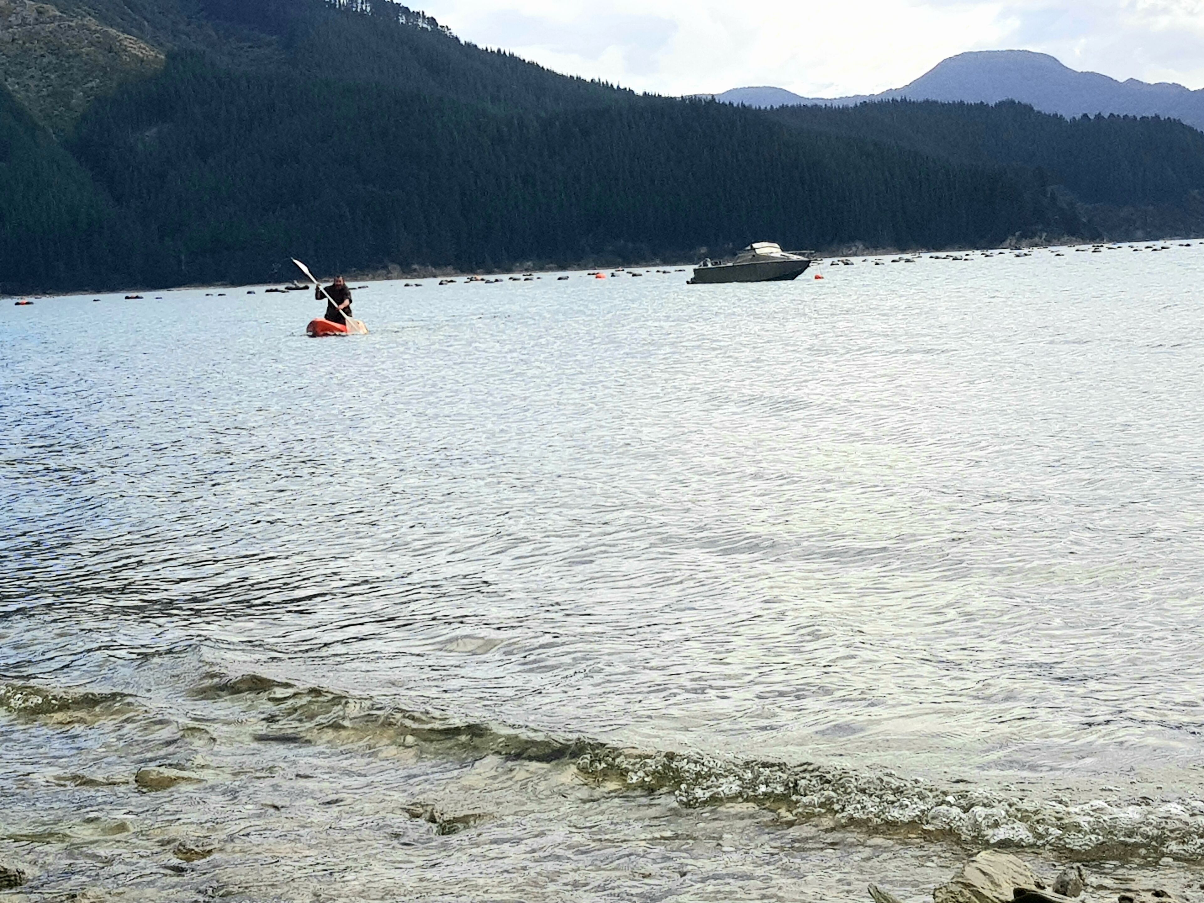 A kayaker on a calm lake with a forested mountain in the background.