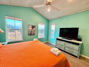 Ein Schlafzimmer mit einem Bett, einem Fernseher, einem Deckenventilator und Fenstern mit Blick ins Freie.