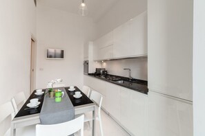 Una cocina moderna con armarios blancos, encimera negra y una mesa de comedor con sillas blancas y una planta verde.