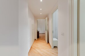 Un pasillo estrecho con suelo de madera, paredes blancas y una puerta que da a un baño.