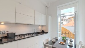 A modern kitchen with white cabinets, a black countertop, and a dining area with a table set for two. - Contemporary Flat at Trastevere (Roma)