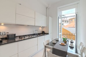 A modern kitchen with white cabinets, a black countertop, and a dining area with a table set for two. - Contemporary Flat at Trastevere (Roma)