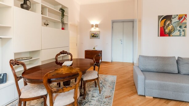 A dining area with a wooden table and chairs, a grey sofa, and a white shelving unit with decorative items. - Contemporary Flat at Trastevere (Roma)