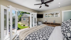 A bedroom with a bed, a ceiling fan, a TV, and a sliding glass door leading to a garden.