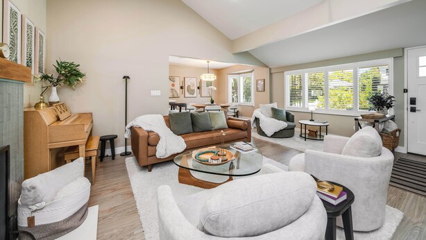 A spacious living room with a piano, sofas, a glass coffee table, and a dining area with a table and chairs.