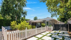 A residential property with a white picket fence, a paved driveway with a geometric pattern, and a house with a covered porch.