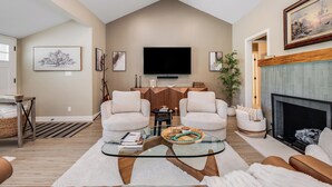 A living room with two sofas, a glass coffee table, a fireplace, and a television mounted on the wall.