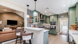 A modern kitchen with a central island, bar stools, and a dining area with a sofa.