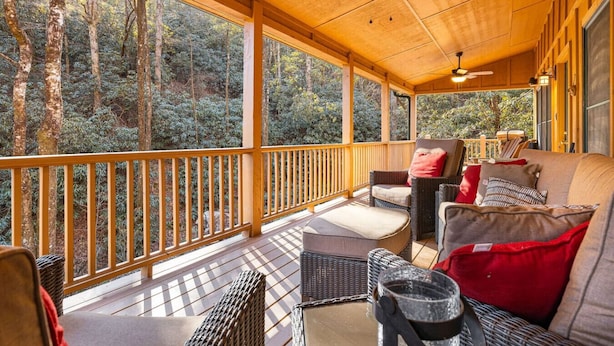 A covered porch with wooden railings, wicker furniture, and a ceiling fan.