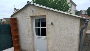 Een laag, eenlaags gebouw met een witte deur en een raam, een houten plank en een zwarte mat bij de ingang.
