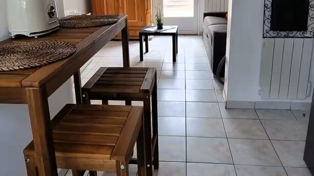 Een ruime keuken met een houten eettafel en stoelen, een groot houten kast en een betegelde vloer.