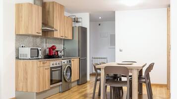 Cuina moderna amb armaris de fusta, un frigorífic d'acer inoxidable, microones, torradora i rentadora. Hi ha una zona de menjador amb taula i cadires.