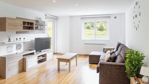 Un salon moderne doté d’un téléviseur à écran plat, de meubles en bois, d’un canapé gris et d’une fenêtre donnant sur un paysage verdoyant.