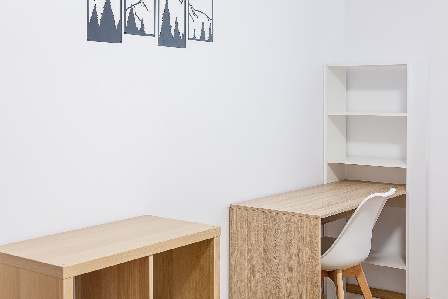 Un espacio de estudio con un escritorio de madera, una silla blanca y una estantería blanca.