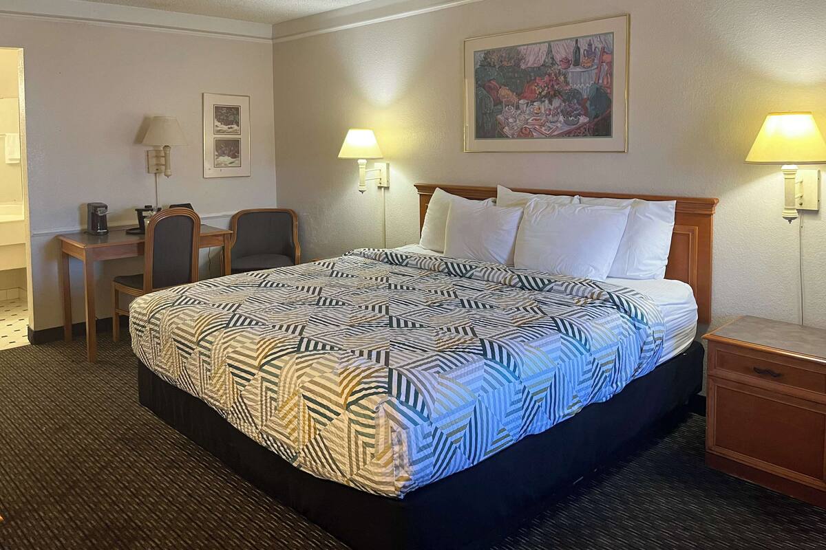 Ein Hotelzimmer mit einem großen Bett, zwei Nachttischlampen, einem Schreibtisch mit Stuhl und einem Bild an der Wand.