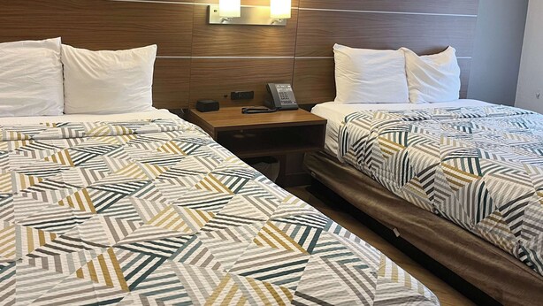 A hotel room with two beds, each with patterned bedding, a wooden headboard, bedside lamps, and a nightstand with a phone and a small table. - Studio 6 Phoenix, AZ - Midtown (Phoenix)