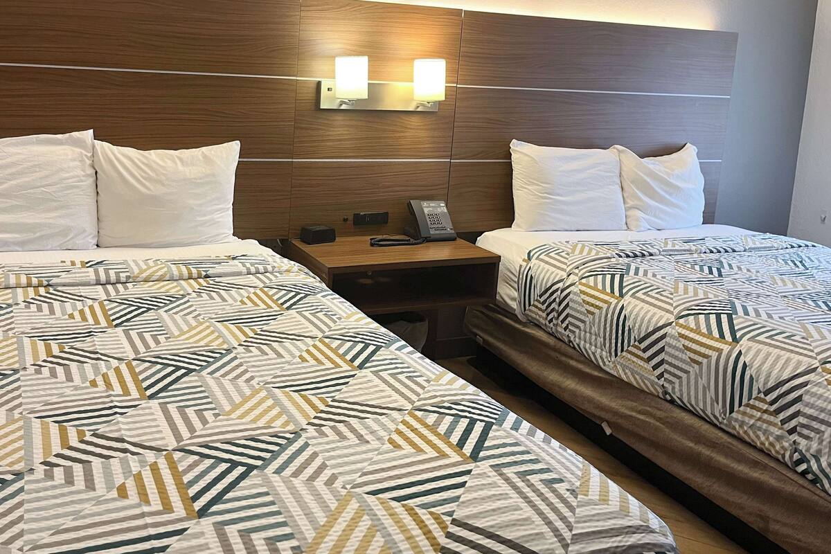 Ein Hotelzimmer mit zwei Betten, jeweils mit gemusterten Bettbezügen, einem Holzkopfende, Nachttischlampen und einem Nachttisch mit Telefon und kleinem Tisch.