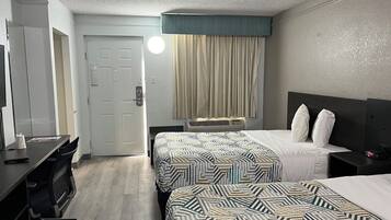 A hotel room with two beds, a desk, a chair, a TV, and a window with curtains.