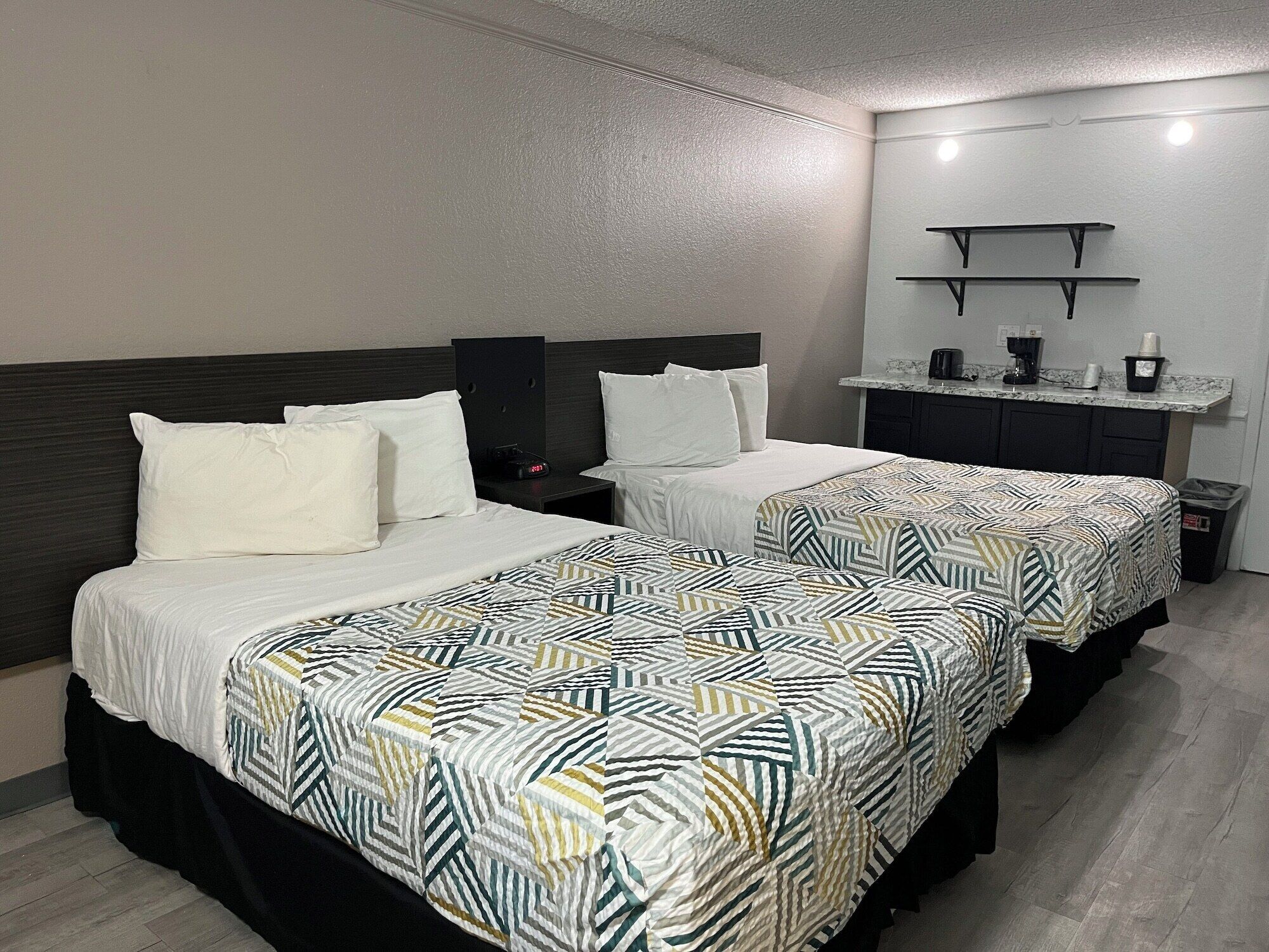 A hotel room with two beds, a small kitchenette, and a bathroom.