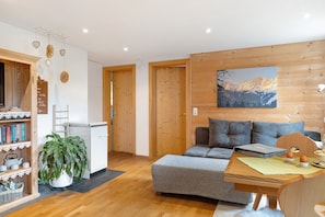 En hyggelig stue med en sofa, et spisebord med bordskåner, en bogreol og en potteplante.