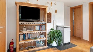 Ein Wohnzimmer mit Fernseher, Bücherregalen, einer Pflanze, einem Feuerlöscher und einem Kühlschrank.