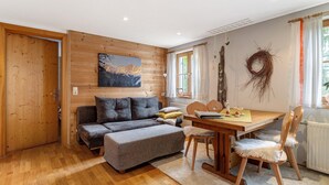 Ein gemütliches Zimmer mit Holzboden, einer Couch, einem Esstisch mit Stühlen und einem an der Wand hängenden Bild.