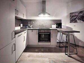 A modern kitchen with a built-in oven, a stainless steel range hood, and a bar stool.