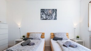 A twin room with two beds, each with a patterned bedspread, bedside tables with lamps, a wall-mounted artwork, and a wooden floor. - Room 'Doppelzimmer 2' with Shared Terrace, Shared Garden and Wi-Fi (Dielheim)