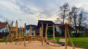 A playground with wooden structures, a bench, and houses in the background. - Room 'Doppelzimmer 2' with Shared Terrace, Shared Garden and Wi-Fi (Dielheim)