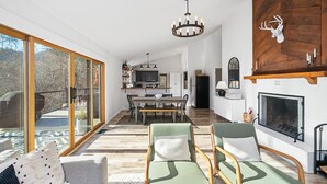 En rummelig opholdsstue med pejs, store vinduer og et spiseområde.