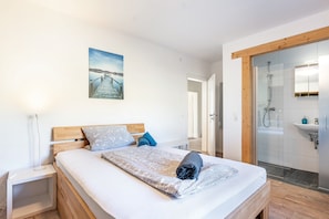 Een slaapkamer met een bed, een nachtkastje, een badkamer met douche en een aan de muur hangend schilderij.