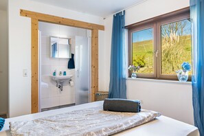 A bedroom with a bed, a window with a view of greenery, a bathroom with a sink and mirror, and wooden beams on the ceiling. - Room 'Einzelzimmer' with Shared Terrace, Shared Garden and Wi-Fi (Dielheim)