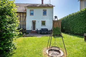 Una casa de dos pisos con fachada blanca, una chimenea y un pequeño porche con mobiliario exterior.