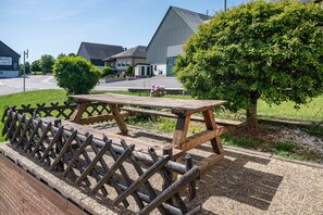 A picnic table with a wooden bench, surrounded by a metal fence, in a grassy area with a building in the background.
