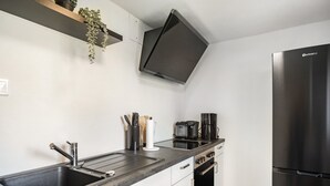 Moderni keittiö, jossa on ruostumattomasta teräksestä valmistettu allas, musta jääkaappi ja sisäänrakennettu uuni.