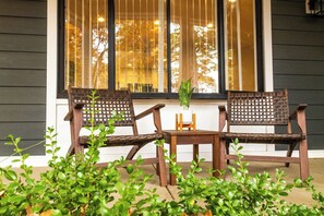 Een veranda met twee houten stoelen en een kleine tafel, omringd door groene planten.