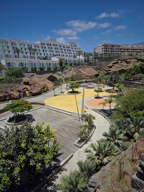 A landscaped area with a central circular plaza, surrounded by buildings with balconies and a mountainous backdrop.