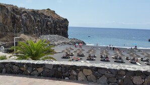 Une plage bordée de murets en pierre, avec des parasols et des chaises longues.