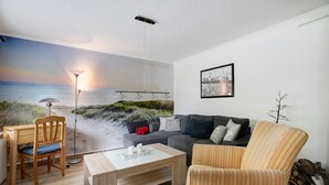 A living room with a beach mural, a sofa, a striped armchair, a coffee table, and a desk with a chair. - Holiday Home 'Gerda' with Private Terrace, Private Garden and Wi-Fi (Stadum)