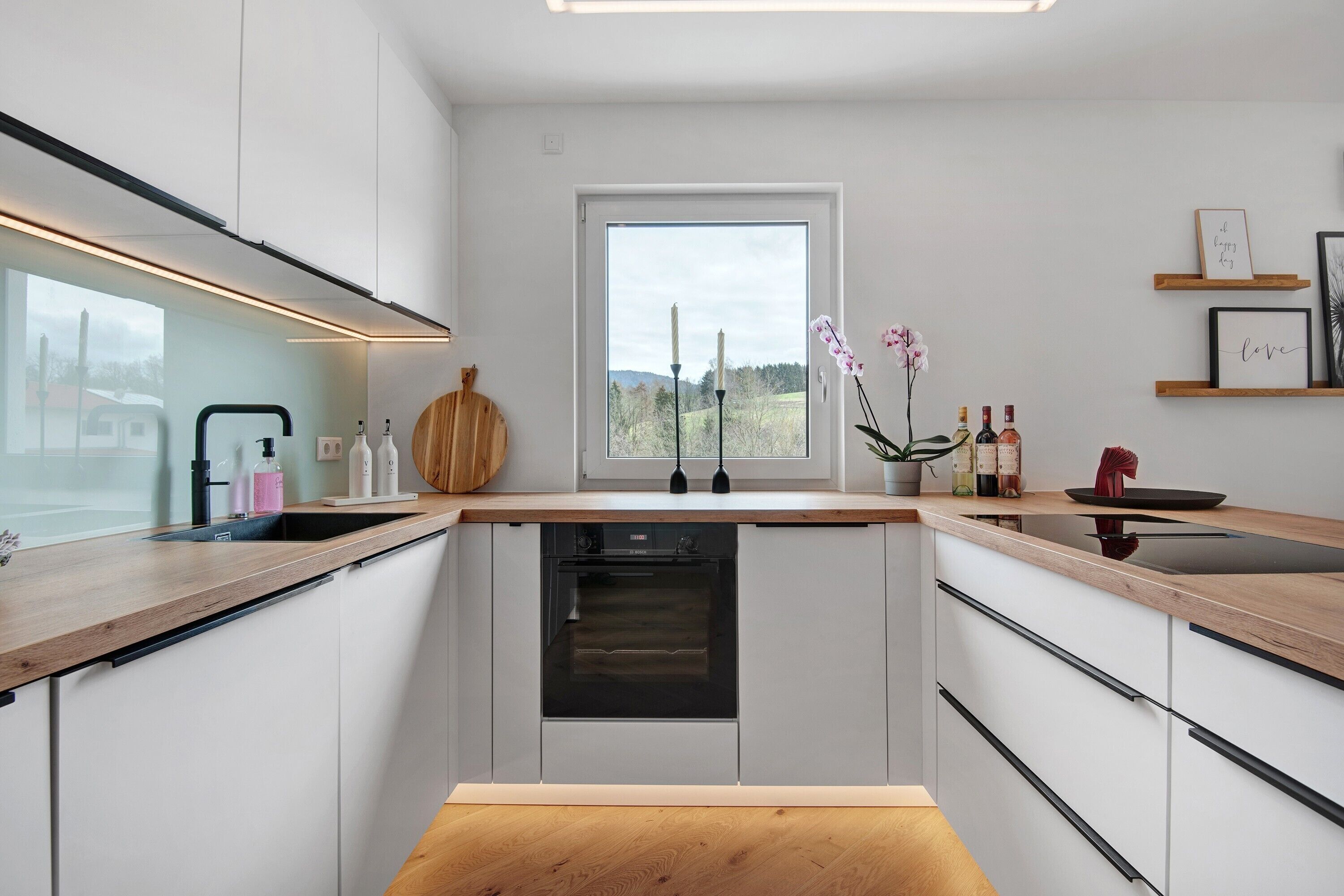 A modern kitchen with a built-in oven, a window with a view, and a wooden countertop.