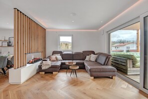 Uma sala de estar moderna com um sofá seccional, uma parede de destaque em madeira, uma lareira e uma janela grande.